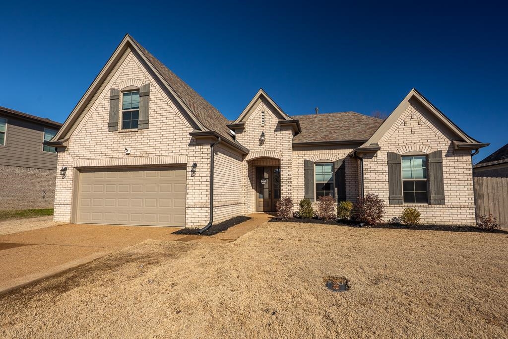French country inspired facade featuring brick siding, concrete driveway, roof with shingles, and a garage