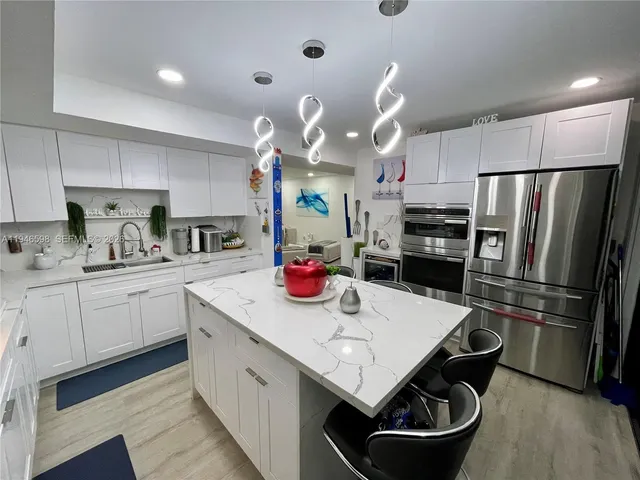 a kitchen with stainless steel appliances a sink a stove a refrigerator cabinets and chairs