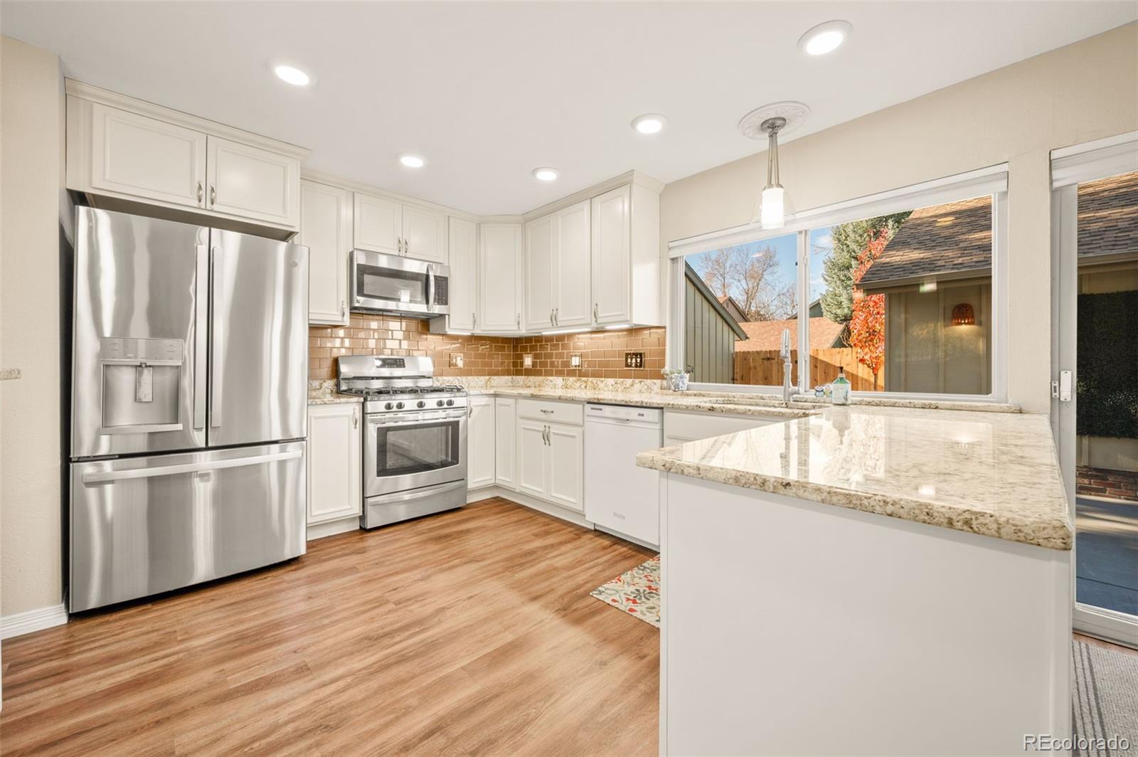 8734 Independence Way Arvada, CO 80005 - Photo 9 of 50 a kitchen with stainless steel appliances granite countertop a refrigerator a sink dishwasher a stove and white countertops with wooden floor