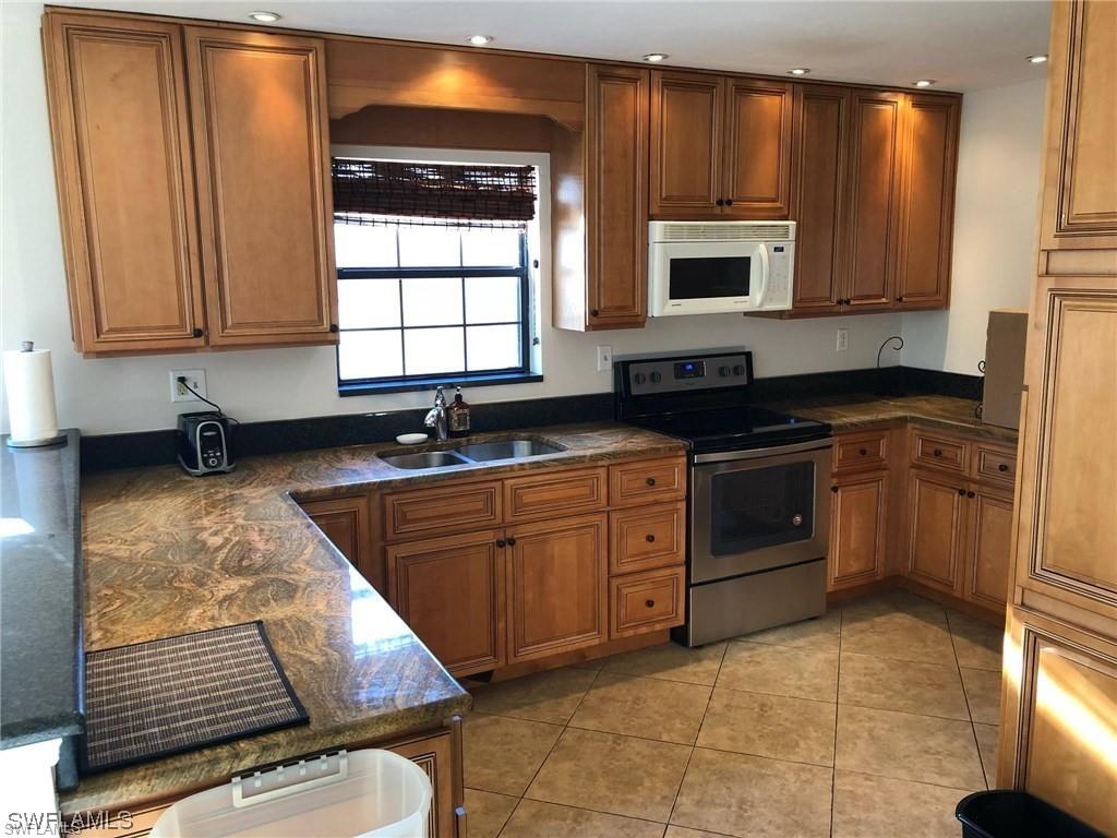 5270 Treetops Drive, Unit J201 Naples, FL 34113 - Photo 3 of 6 Kitchen with stainless steel range with electric cooktop, white microwave, dark stone counters, brown cabinets, and recessed lighting