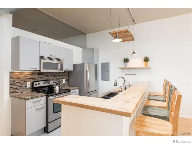 a kitchen with stainless steel appliances kitchen island granite countertop a refrigerator a stove a sink and white cabinets with wooden floor