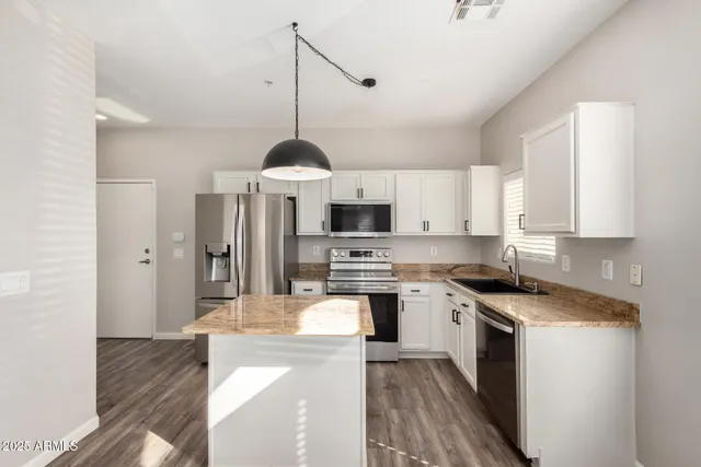 a kitchen with stainless steel appliances granite countertop a stove top oven a sink a refrigerator and white cabinets with wooden floor