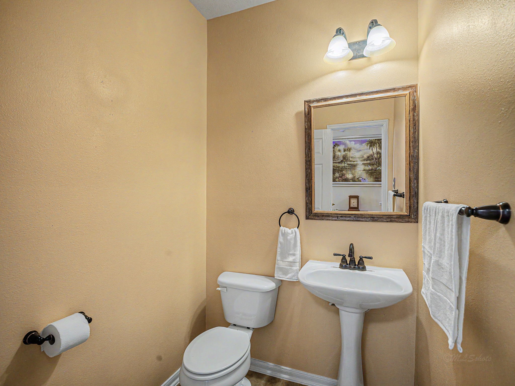 2210 Fox Path Katy, TX 77494 - Photo 11 of 47 This private half bathroom features a classic pedestal sink accented by rich, oil-rubbed bronze fixtures and a decorative wood-framed mirror with bright vanity lighting.The walls are finished in a soft, warm yellow tone that brings a cheerful, sun-kissed energy to the space, creating an inviting and cozy atmosphere for guests.