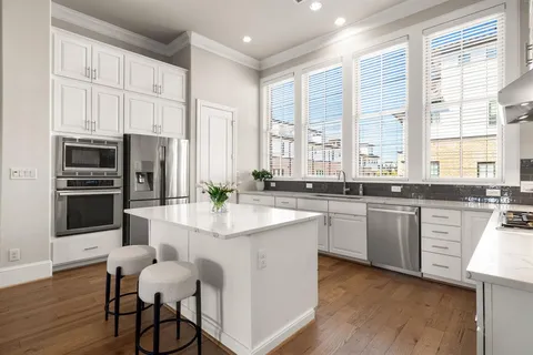 a kitchen with stainless steel appliances granite countertop a stove a sink a refrigerator and white cabinets with wooden floor