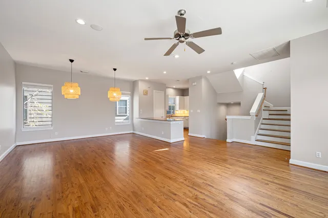a view of an empty room and a kitchen with wooden floor
