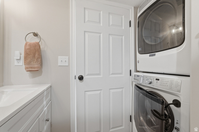 11189 Ohenry Road East Sandy, UT 84070 - Photo 29 of 44 White stacked washer and dryer unit, white six-panel interior door with dark hardware, built-in white vanity with integrated sink, and light neutral-toned walls