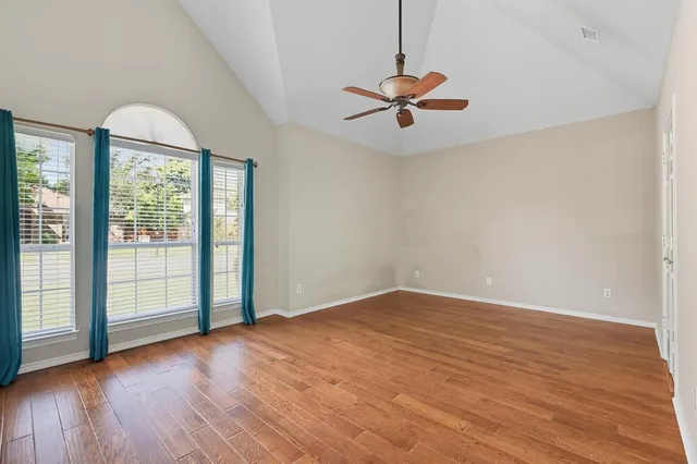 an empty room with wooden floor fan and windows