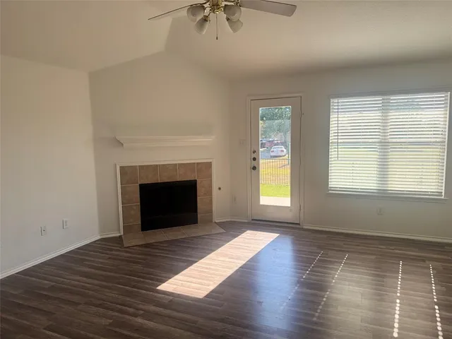 a view of an empty room with wooden floor fireplace and a window