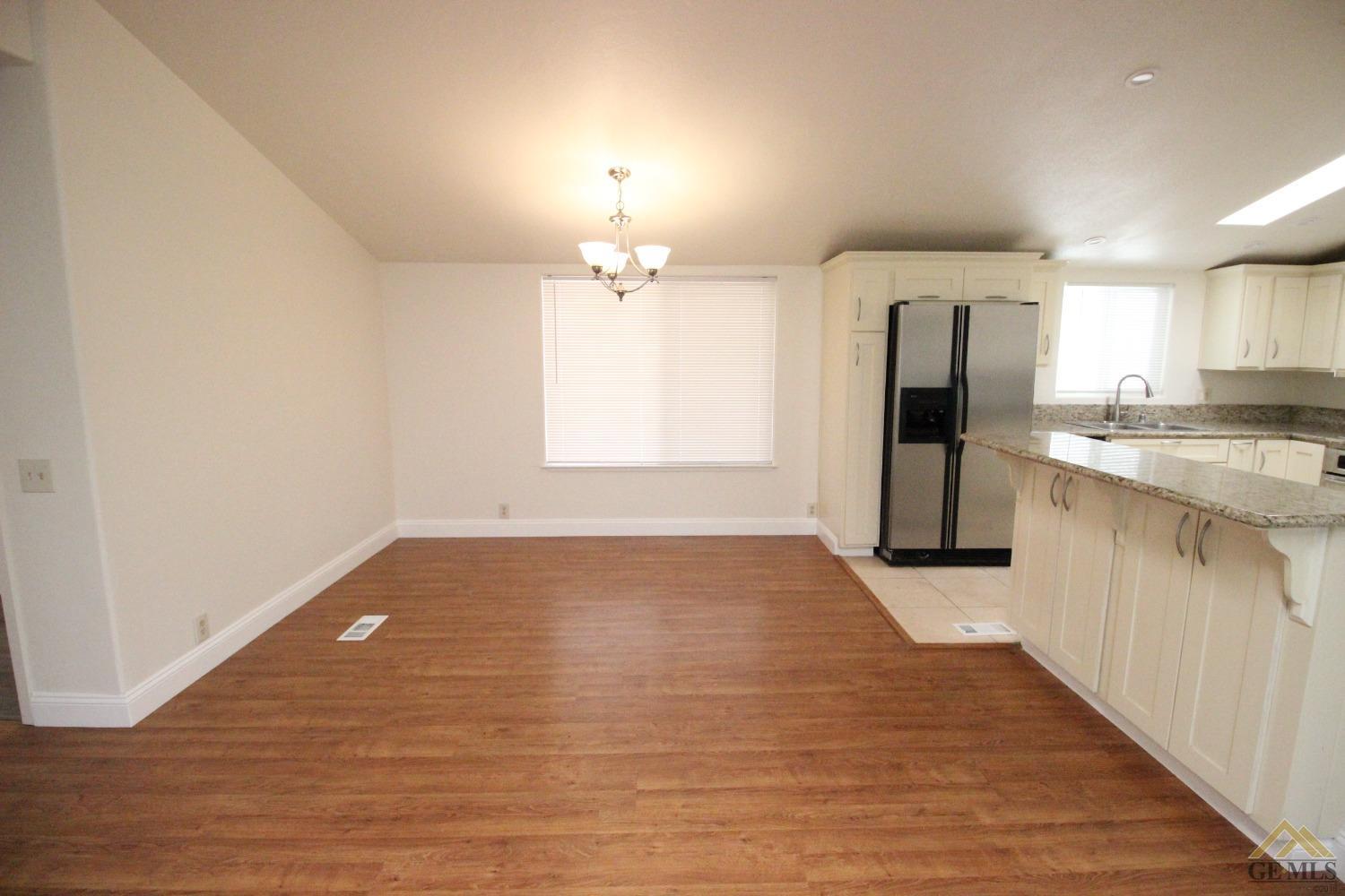 Undisclosed Address Bakersfield, CA 93308 - Photo 9 of 26 an empty room with wooden floor and kitchen view