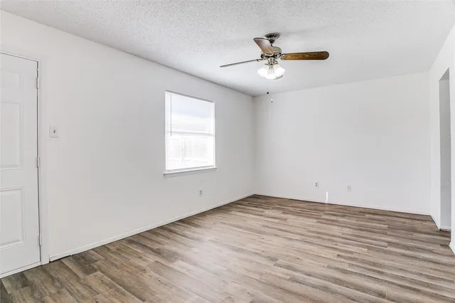 an empty room with wooden floor chandelier fan and windows