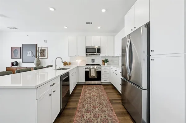 a kitchen with stainless steel appliances kitchen island granite countertop a refrigerator a stove a sink a dining table and chairs with wooden floor