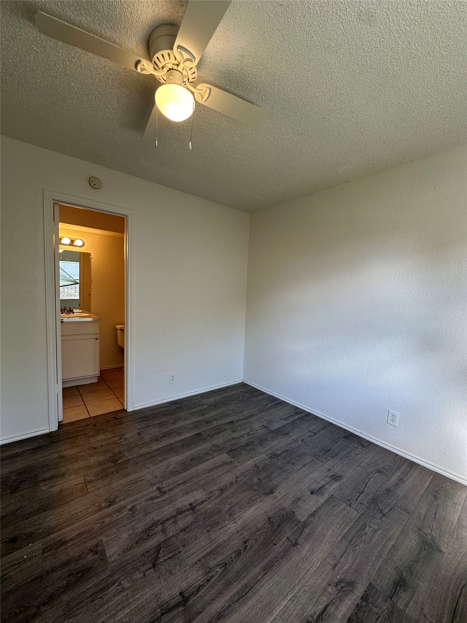 6906 Deep Circle, Unit B Austin, TX 78744 - Photo 18 of 19 Unfurnished bedroom with a textured ceiling, a ceiling fan, dark wood-type flooring, and connected bathroom