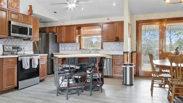 a kitchen with stainless steel appliances granite countertop a stove top oven a refrigerator a dining table and chairs with wooden floor