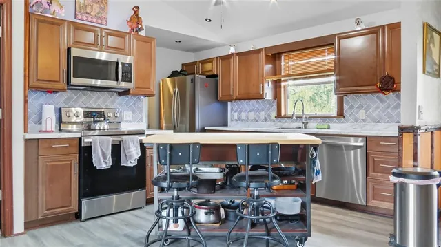 a open kitchen with stainless steel appliances granite countertop a stove top oven a sink a dining table and chairs with wooden floor