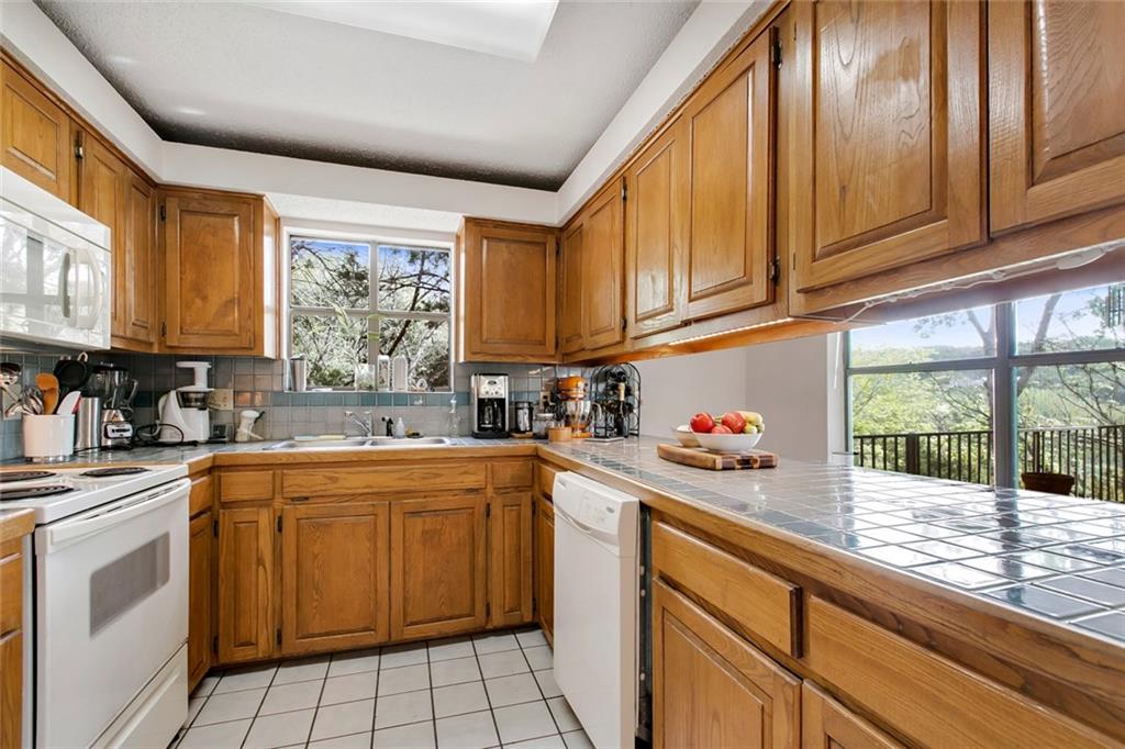 9201 Simmons Road, Unit 117 Austin, TX 78759 - Photo 6 of 11 Kitchen featuring wood cabinetry, tiled countertops, and white appliances