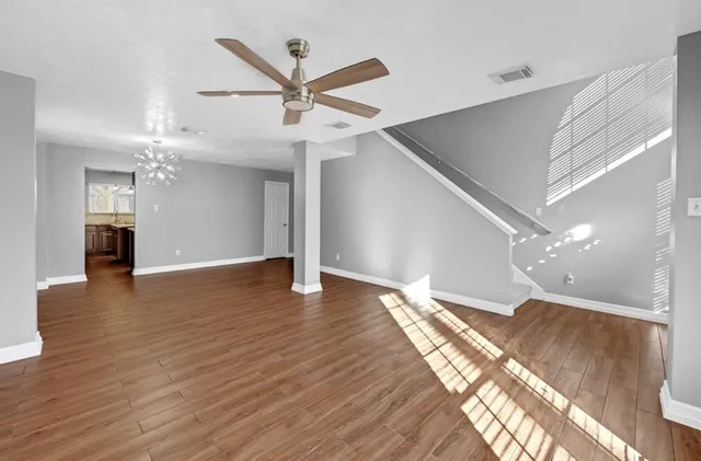 a view of an empty room with wooden floor and a ceiling fan