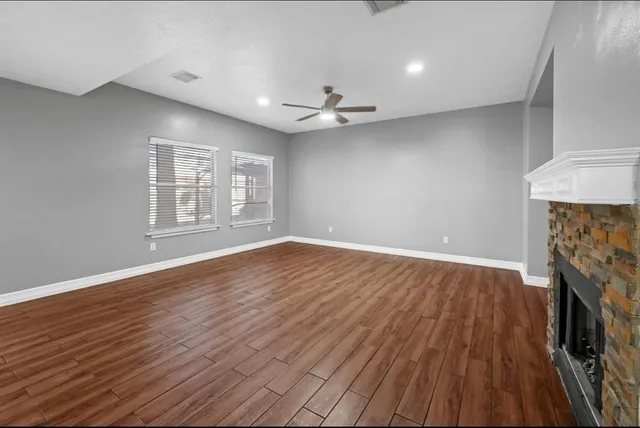an empty room with wooden floor fireplace and windows