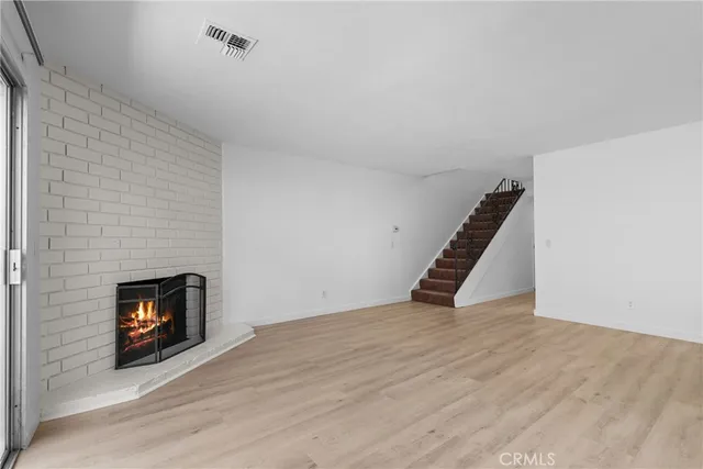 a view of an empty room with wooden floor fireplace and a window