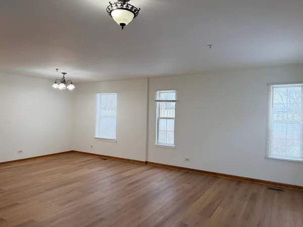 an empty room with wooden floor chandelier fan and windows