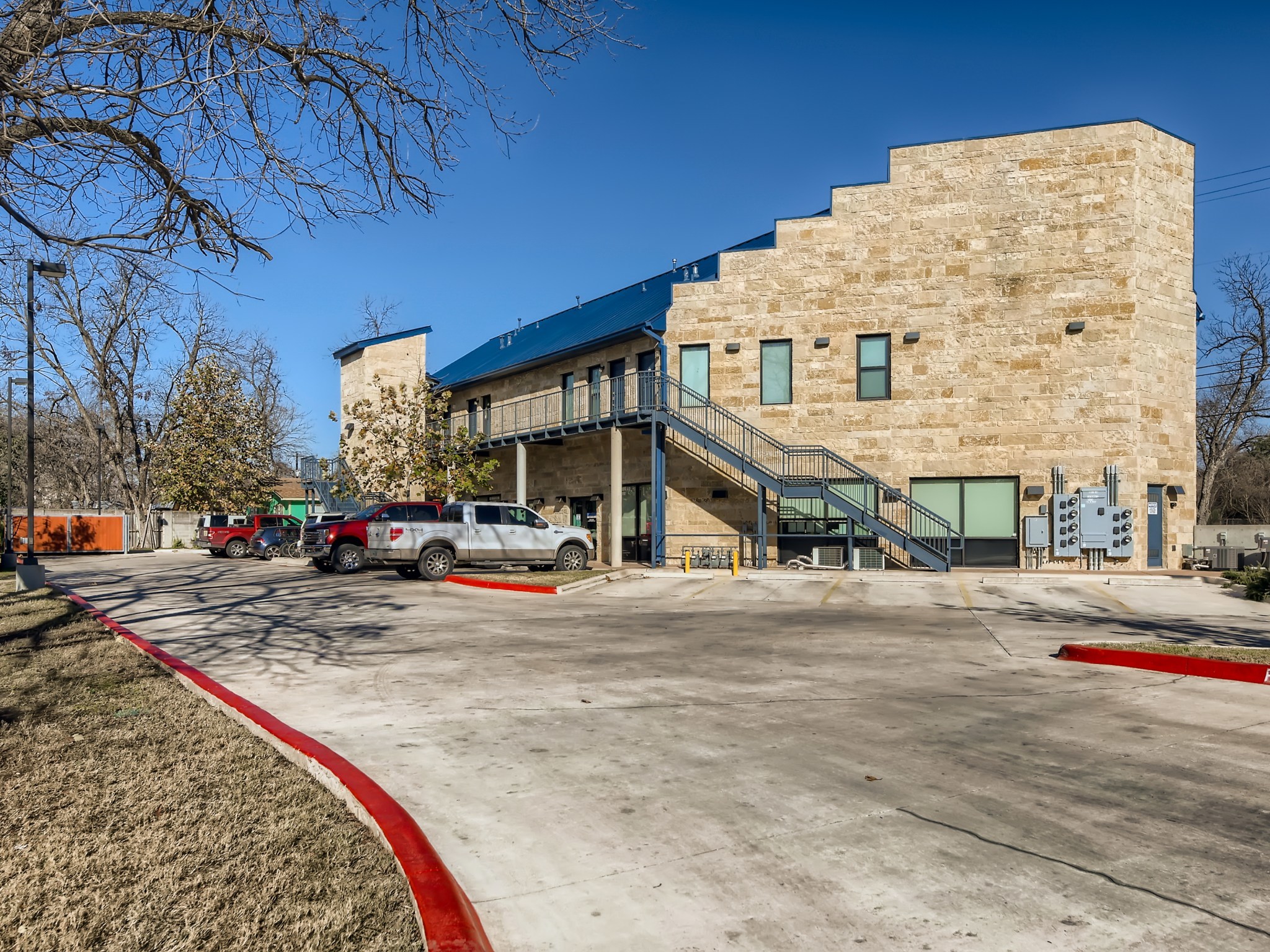 Multi-story commercial building featuring a stone block facade, a blue metal roof, and an exterior metal staircase