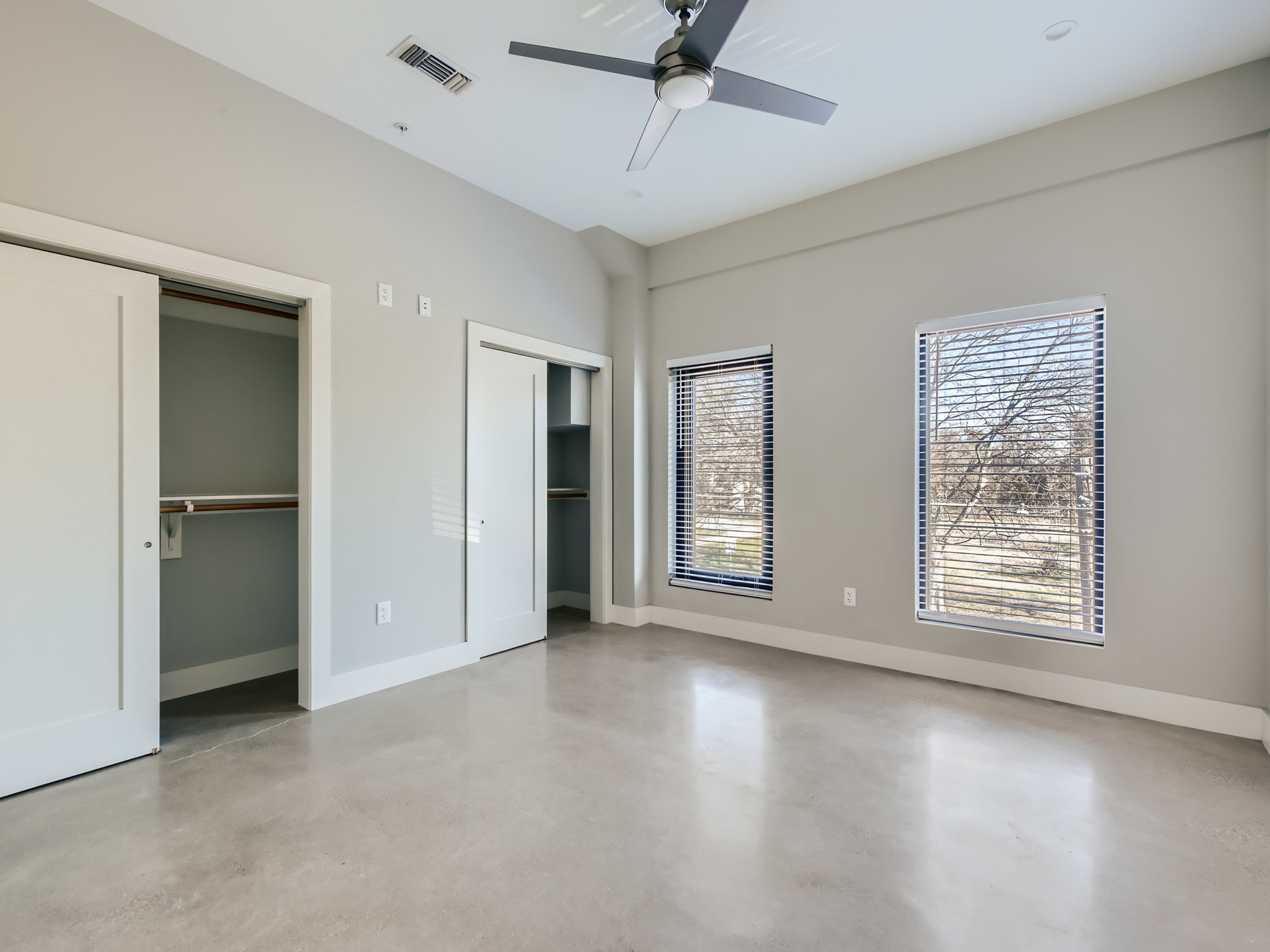 3523 Gonzalez Street, Unit 200 Austin, TX 78702 - Photo 7 of 10 Light-filled room featuring polished concrete flooring, two windows with horizontal blinds, a ceiling fan with integrated lighting, and two closets with sliding doors