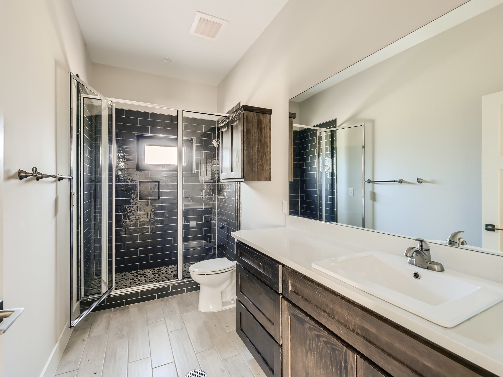 3523 Gonzalez Street, Unit 200 Austin, TX 78702 - Photo 9 of 10 Contemporary bathroom featuring a spacious glass-enclosed shower with dark subway tile, a vanity with a white rectangular sink and light-colored countertop, dark wood-finish cabinetry, and light wood-finish flooring