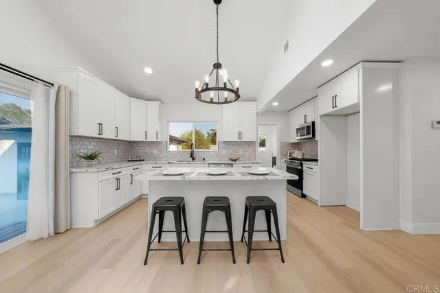 a kitchen with kitchen island stainless steel appliances a dining table chairs sink and cabinets