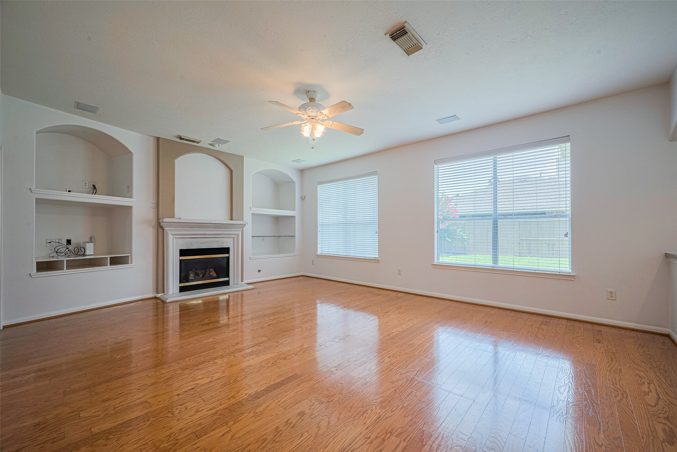 9218 Memorial Pines Way Spring, TX 77379 - Photo 12 of 39 This spacious living room features hardwood floors, a cozy fireplace, built-in shelving, and large windows that let in plenty of natural light. Perfect for relaxation and entertaining.