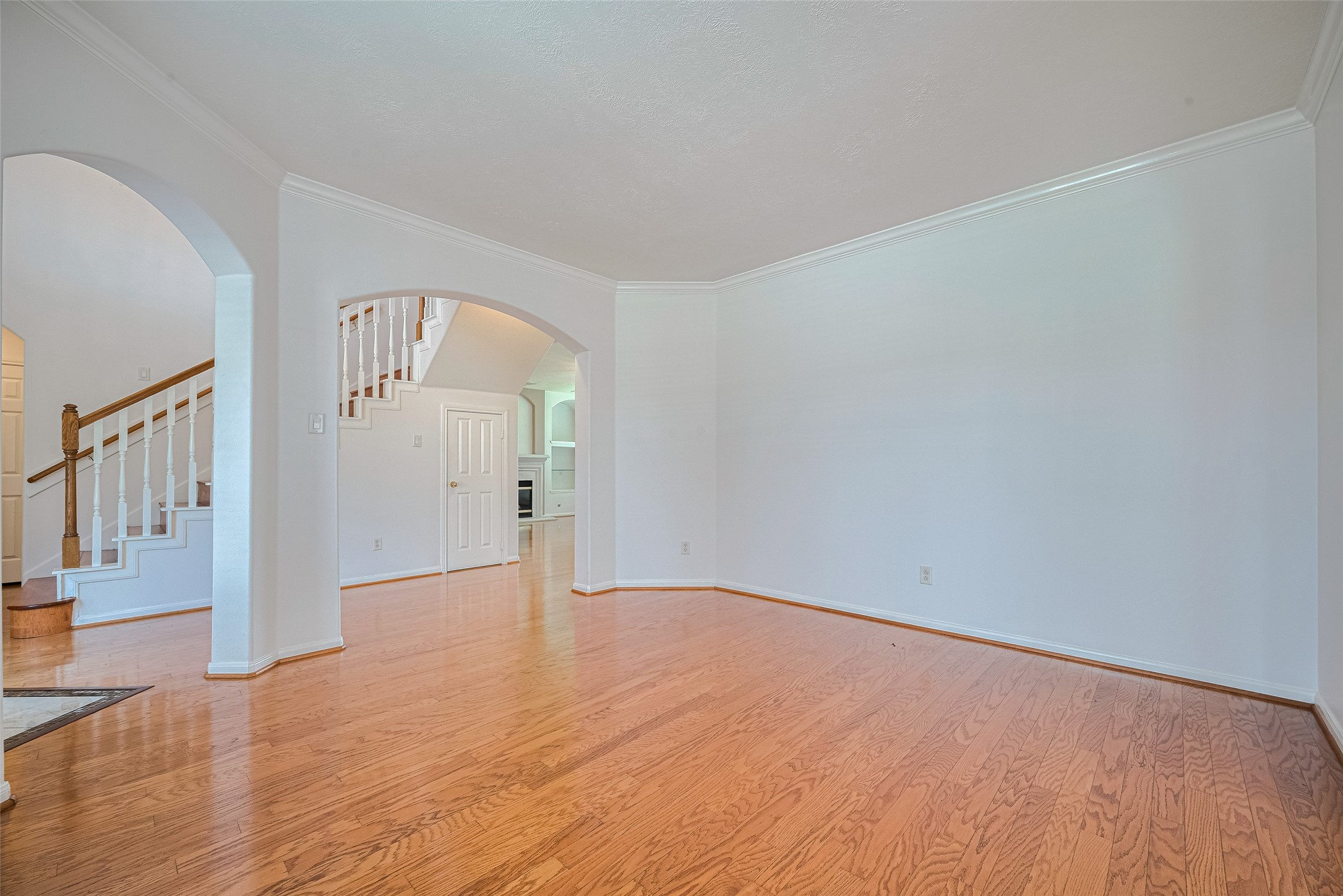 9218 Memorial Pines Way Spring, TX 77379 - Photo 15 of 39 Spacious living room with engineered wood floors, fresh white walls, and elegant archways. It includes a view of an open staircase with wooden railings and leads to the dinning room.