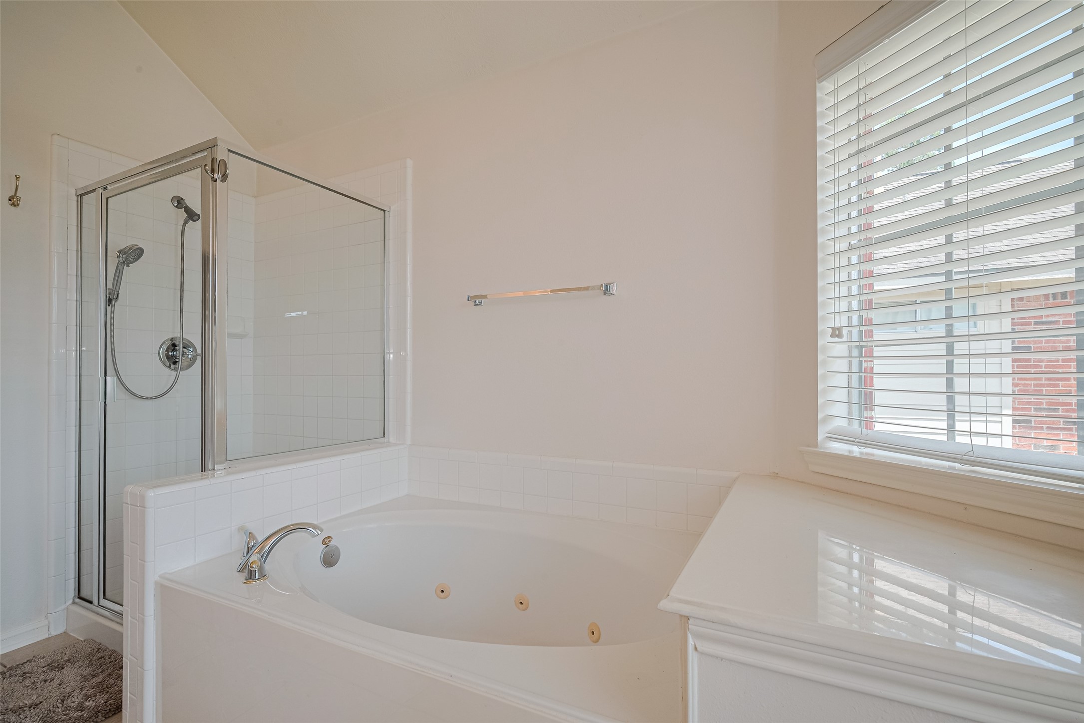 9218 Memorial Pines Way Spring, TX 77379 - Photo 28 of 39 Primary bathroom features a spacious corner bathtub and a separate glass-enclosed shower. Natural light streams through a window with blinds.