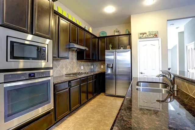 a kitchen with stainless steel appliances granite countertop a refrigerator a stove and a sink