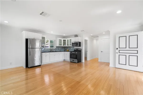 a view of empty room with wooden floor and kitchen