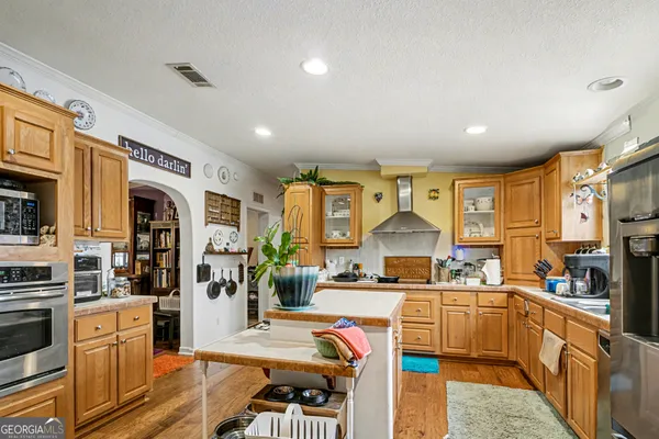 a kitchen with stainless steel appliances kitchen island granite countertop a refrigerator oven a sink dishwasher and white cabinets with wooden floor