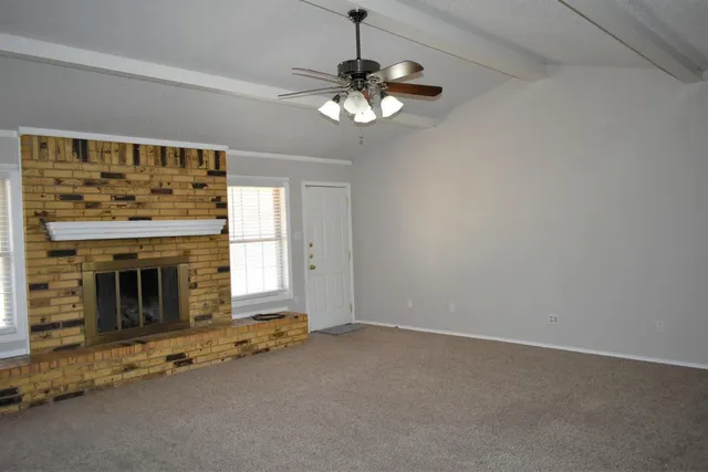 a view of a livingroom with a fireplace a ceiling fan and windows