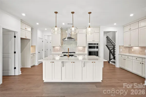 a large kitchen with stainless steel appliances kitchen island granite countertop a refrigerator a sink dishwasher and white cabinets with wooden floor