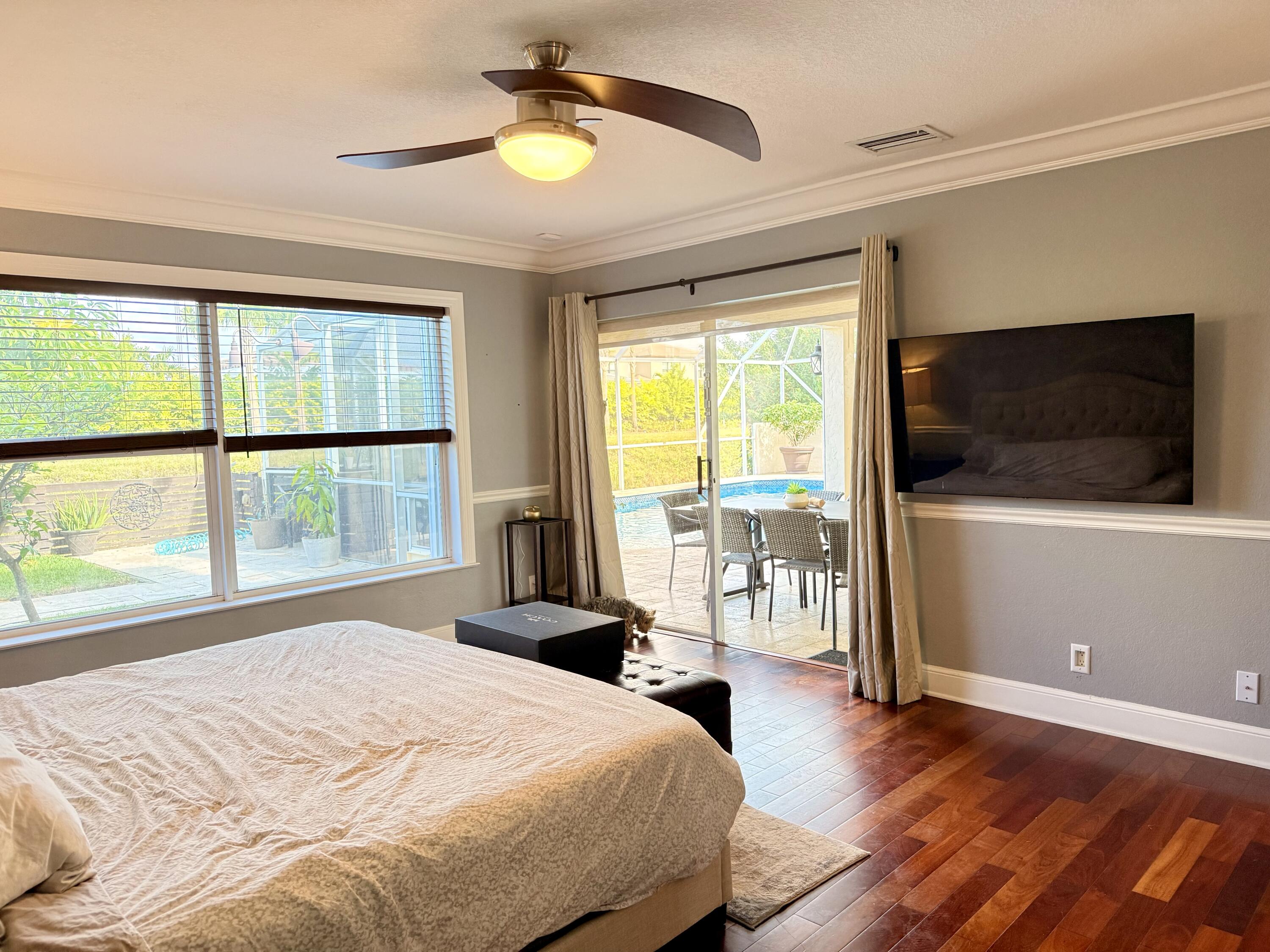 9669 Carousel Circle North Boca Raton, FL 33434 - Photo 17 of 22 a bedroom with a large bed a flat tv screen and a large window with wooden floor