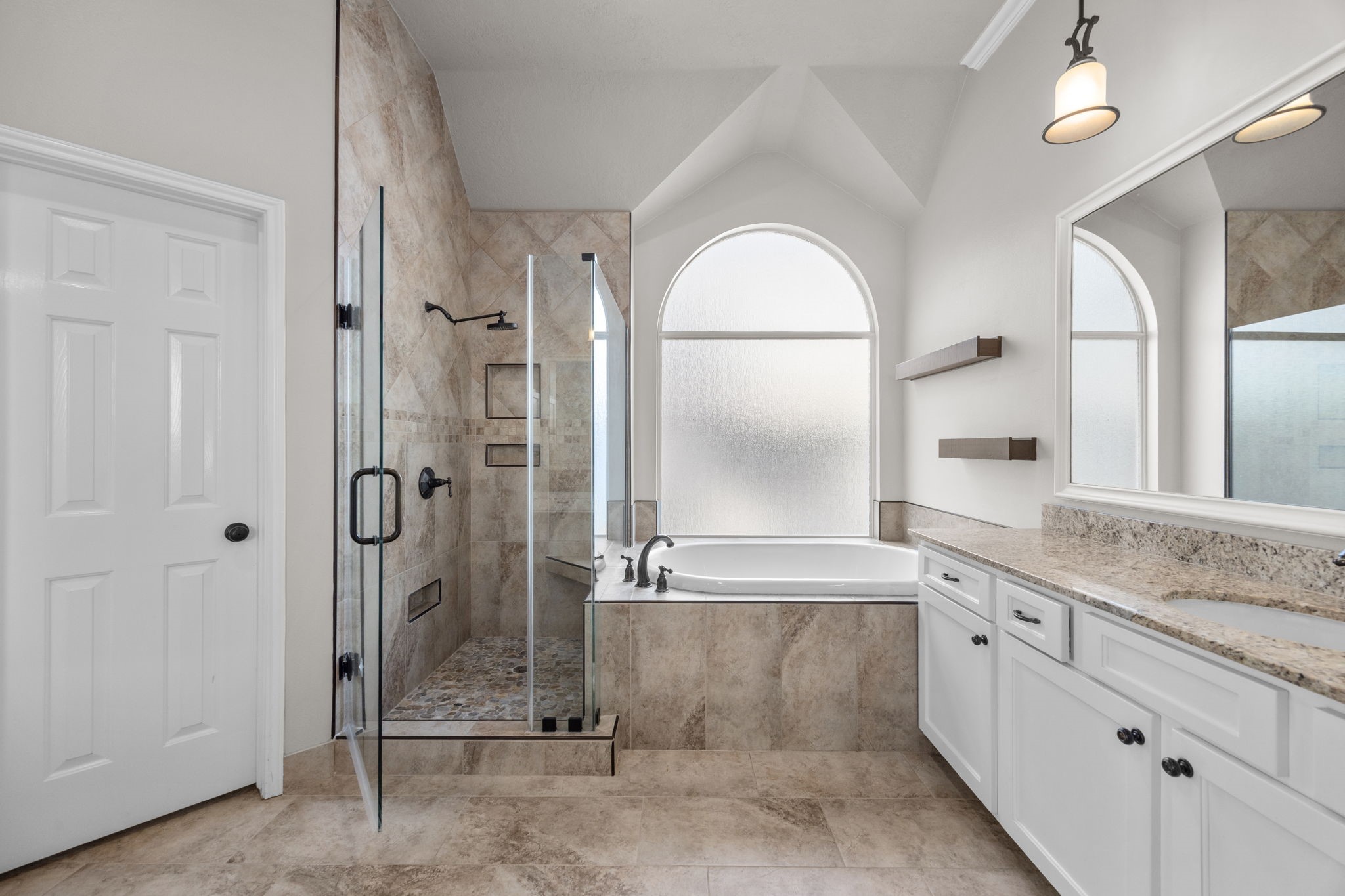 9015 Rhapsody Lane Houston, TX 77040 - Photo 25 of 39 A soaking tub set beneath an oversized arched window, and an updated frameless glass shower with pebble stone flooring.