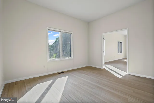 a view of an empty room with window and wooden floor