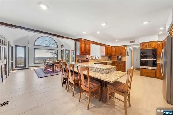 a dining hall with stainless steel appliances granite countertop a stove a refrigerator a oven with a dining table and chairs with wooden floor