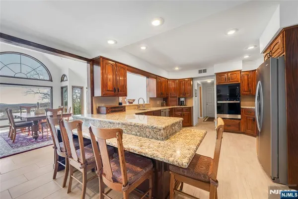 a kitchen with stainless steel appliances granite countertop a kitchen island a stove a table and chairs a refrigerator with wooden floor