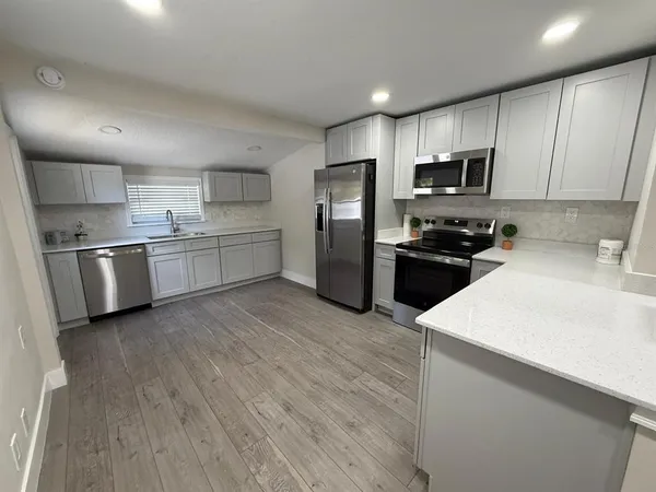 a kitchen with stainless steel appliances a stove top oven a sink dishwasher a refrigerator and white cabinets with wooden floor