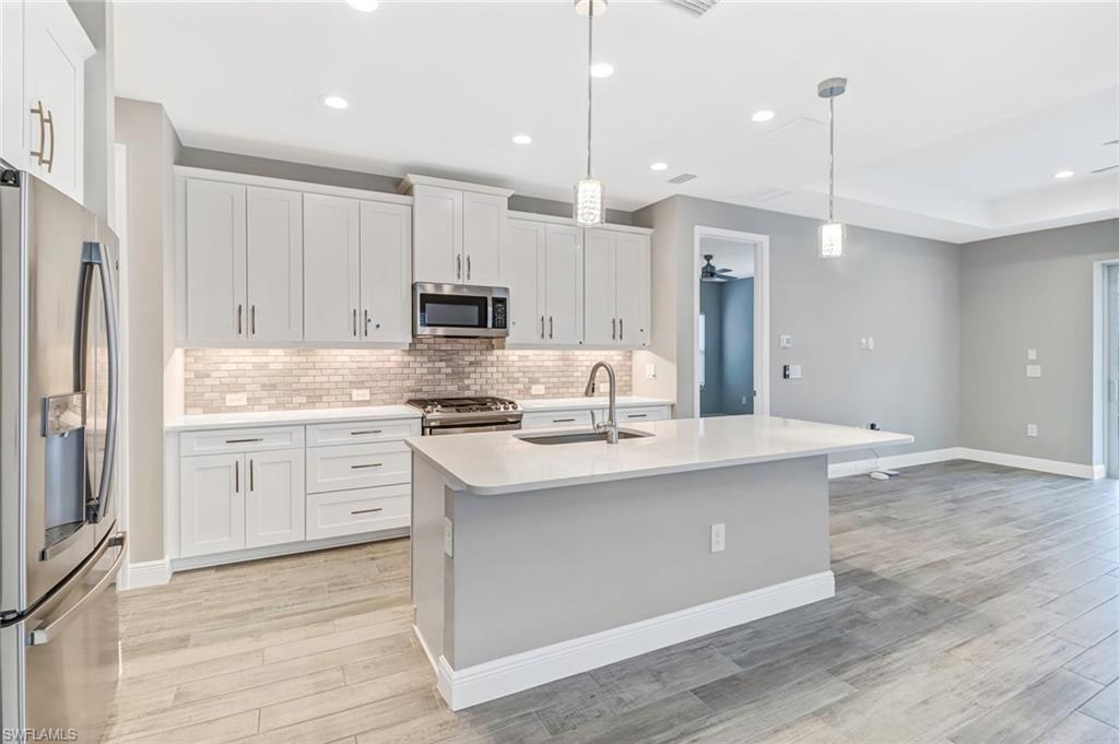 4652 Centaurus Circle Naples, FL 34120 - Photo 3 of 45 Kitchen with stainless steel appliances, white cabinets, light stone countertops, and a kitchen island with sink