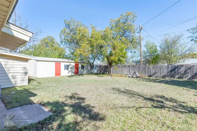a view of a backyard with large trees and wooden fence
