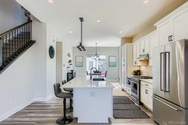 a kitchen with stainless steel appliances a refrigerator a sink dishwasher a stove and white cabinets with wooden floor