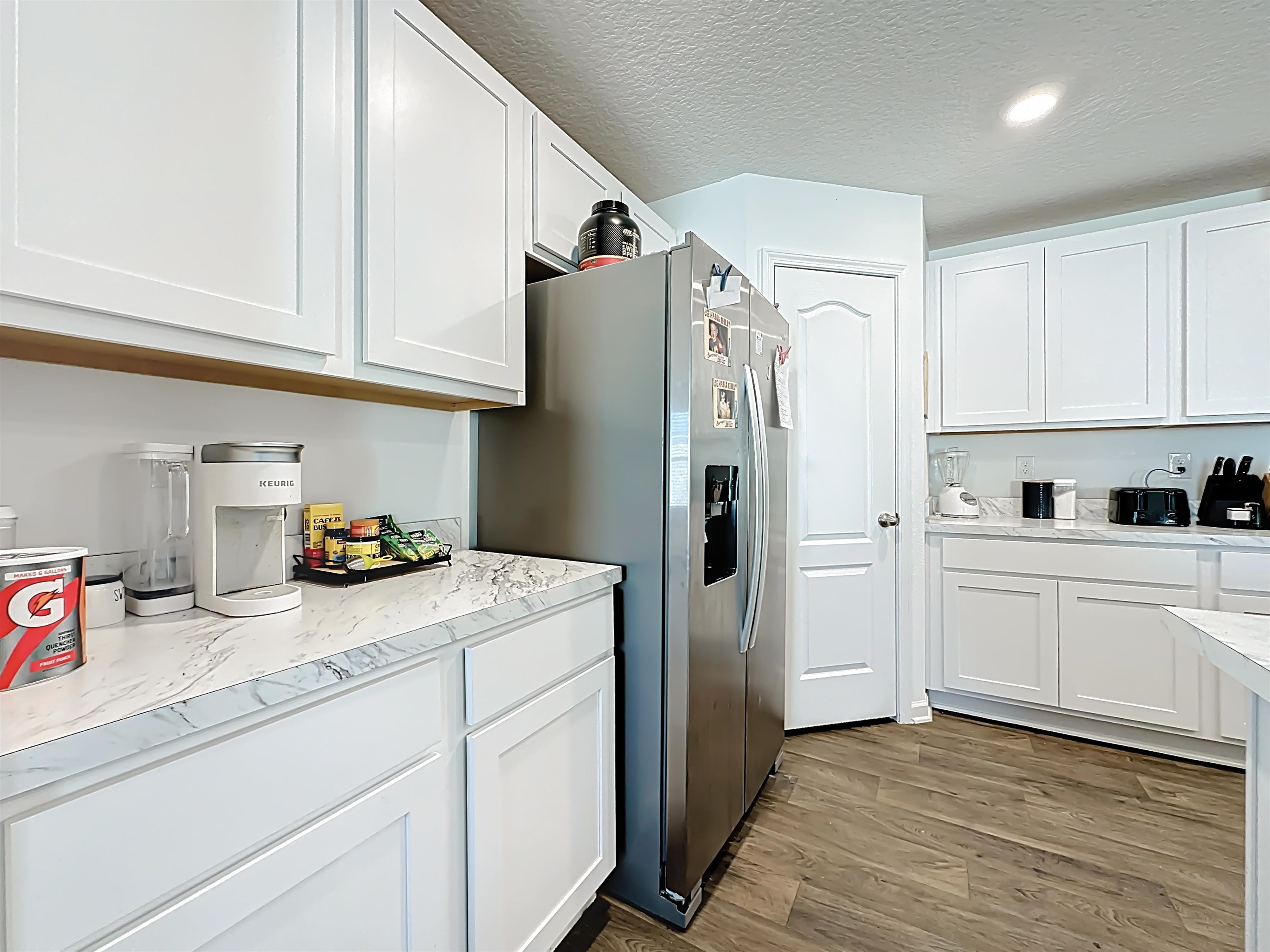 16 Encanto Way Street St. Augustine, FL 32084 - Photo 15 of 56 Kitchen featuring white cabinets, stainless steel refrigerator with ice dispenser, light wood-style flooring, a textured ceiling, and light stone counters