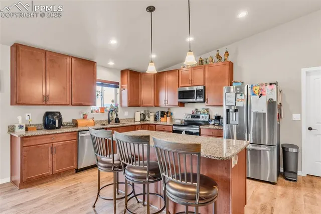 a kitchen with stainless steel appliances granite countertop a stove top oven a refrigerator a sink and a chairs