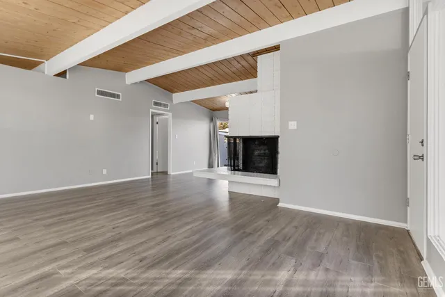 a view of an empty room with wooden floor fireplace and a window