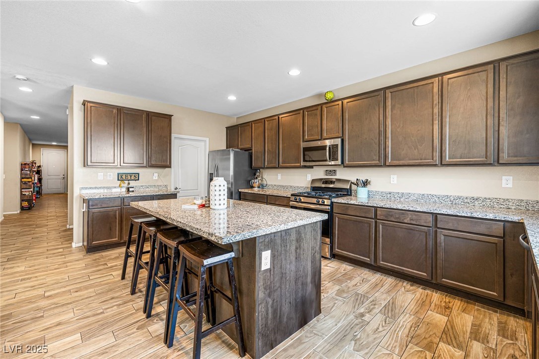10523 Laurel Mountain Lane Las Vegas, NV 89166 - Photo 6 of 36 Kitchen with stainless steel appliances, a kitchen breakfast bar, recessed lighting, dark brown cabinetry, and light wood finished floors