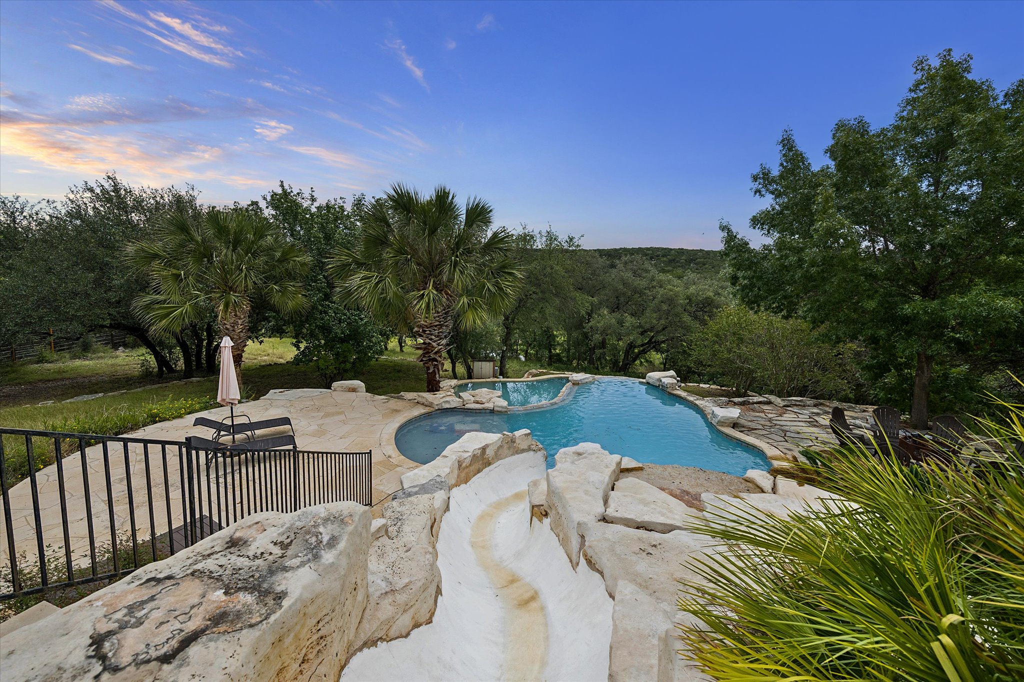 3719 Bee Creek Road Spicewood, TX 78669 - Photo 35 of 40 An inviting pool area with a water slide descends into a verdant landscape.