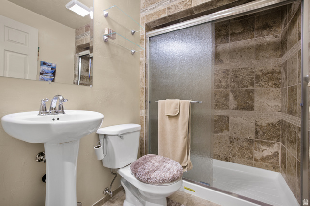 2005 Redtail Way Layton, UT 84040 - Photo 19 of 37 Bathroom featuring a pedestal sink, chrome faucet, wall-mounted mirror with integrated lighting, and a walk-in shower with stone tile surround and frosted glass sliding door